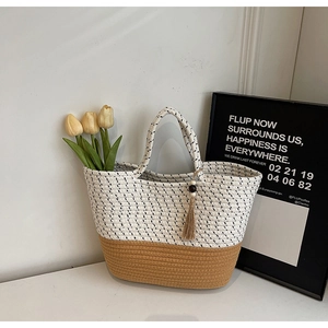 Close-up of a two-tone woven straw tote bag with elegant tassel detail and floral accents