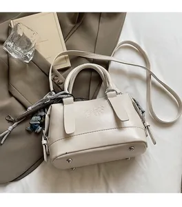 Detail view of cream Boston bag with embossed lettering and decorative charm accessories