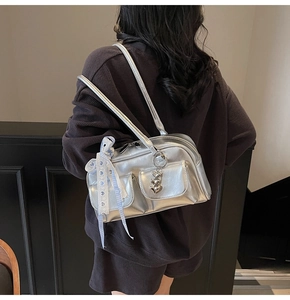 Detail of silver metallic Boston bag with heart charm and ribbon on model's shoulder
