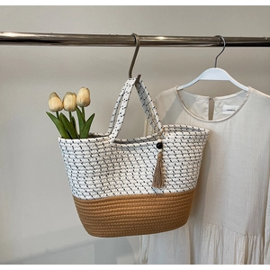 Detail of a woven tote bag with contrast patterns and decorative tassel charm