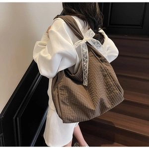 Detail of coffee plaid tote bag featuring a white lace bow on the shoulder strap