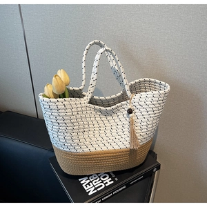 Detail of color-block woven tote bag with fringe charm and wood bead on elegant books