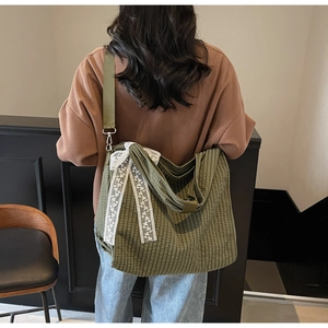 Detail of green checkered canvas tote bag with a white lace bow and adjustable strap
