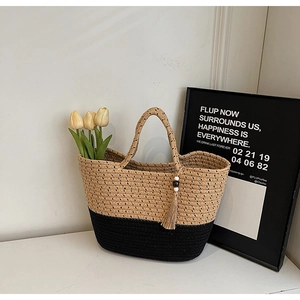 Detail of two-tone straw tote bag with black contrast bottom and decorative tassel charm