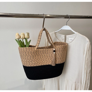 Detail view of woven straw tote bag featuring tassel charm and interior tulip accents