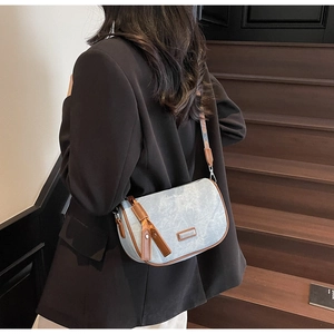 Detail of light blue denim crossbody bag with brown leather trim and jacquard strap