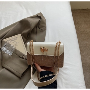 Détail du sac beige à chaîne avec fermoir chat et sequins sur literie blanche