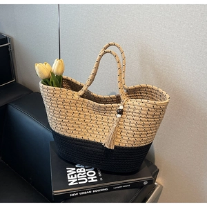 Detail view of a woven tote bag with contrast stitching and beaded tassel on a sofa