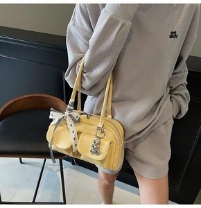 Detail of yellow minimalist shoulder bag with heart charm and ribbon on leather handle
