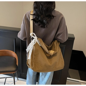 Detail of checkered canvas hobo bag featuring lace bow and wide fabric shoulder strap