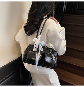 Close-up of black glossy shoulder bag with buckle pockets and a blue plaid bow