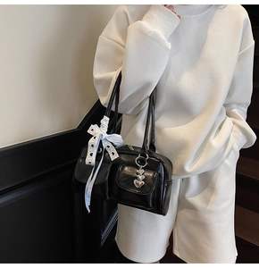 Detail of glossy black shoulder bag featuring dual buckle pockets and heart pendant