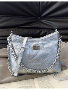 Silberne Stepptasche mit Metallkette und Drehverschluss auf grauem Stoffhintergrund