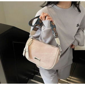 Detail of pink half-moon bag featuring ethnic floral strap and metallic nameplate