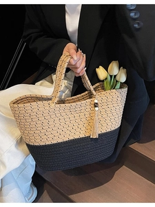 Chic woven straw tote bag with black contrast stitching and decorative tassel charm