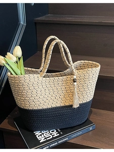 Chic two-tone straw woven tote bag with fringe charm on a stylish wooden staircase