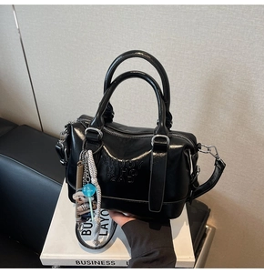 Detail of black glossy leather pillow bag with embossed letters and silver hardware accents