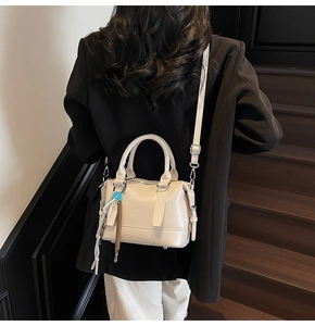 Detail of beige Boston handbag featuring textured embossing and blue beaded charm