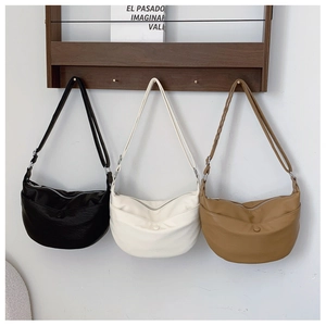 Detailed close-up of crescent moon handbags in black, cream, and brown on a wooden hanger