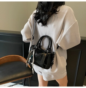 Detail of a black glossy crossbody bag with embossed text and decorative charms on a model