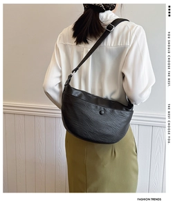 Detail of black leather crescent bag with adjustable strap and silver metal buckle