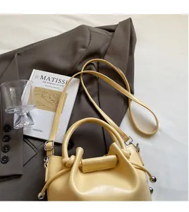 Detail einer cremegelben Kordelzug-Beuteltasche mit Webgriff auf einem braunen Blazer