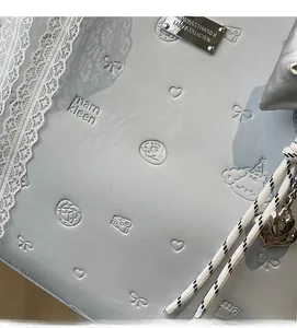 Detail of light blue tote bag featuring embossed patterns, lace trim and silver heart charm