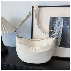 Detail of a creamy beige leather hobo bag with a front pocket on a minimalist table