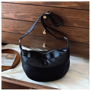 Detail of black pebbled leather crescent bag with adjustable strap and silver zipper closure