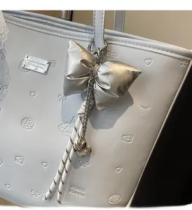 Detail of grey-blue leather tote bag featuring a silver padded bow charm and embossed patterns