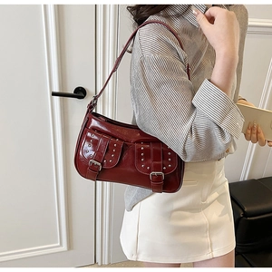 Detail of burgundy rivet shoulder bag with silver buckles and glossy leather finish