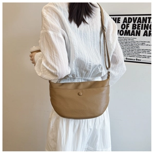 Detail view of a brown faux leather crescent bag with pebble texture on a model