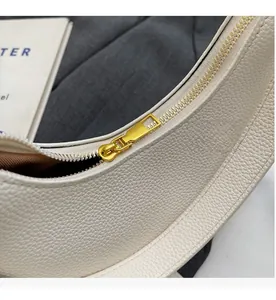 Détail de la fermeture éclair dorée et du cuir grainé sur le sac à bandoulière blanc cassé