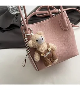 Detail of pink lychee leather bucket bag featuring a cute beige plush bear charm with UVS logo