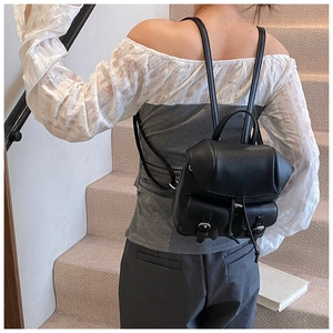 Detail of a black leather mini backpack with metal buckles shown on a model outdoors