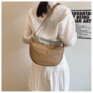 Detail view of khaki half-moon crossbody bag worn over a white striped shirt