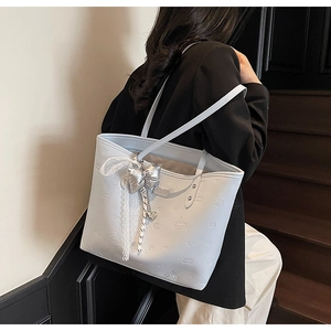 Detail of light blue tote bag featuring embossed patterns and silver bow charm with lace trim