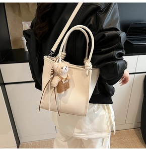 Detail of off-white lychee grain leather tote with knotted ring handle and plush bear charm