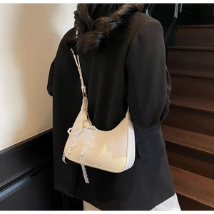 Détail du sac demi-lune crème avec breloque perle et nœud en dentelle sur l'épaule
