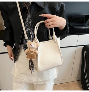 Detailed shot of white litchi leather tote bag with cute bear charm and thin shoulder strap