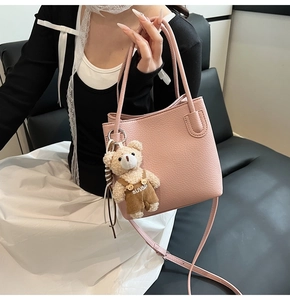 Detailed close-up of pink pebbled leather bucket bag with cute plush bear charm accessory