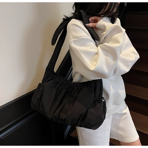 Detail of black pleated cloud bag featuring decorative bow shoulder strap and nylon texture
