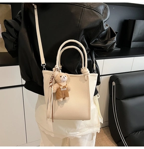 Detail of cream white leather bucket bag with a cute plush bear pendant and long strap