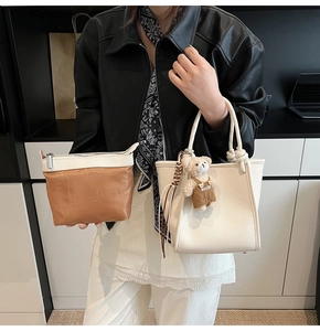 Detail of cream bucket bag with teddy bear charm and brown inner pouch on model
