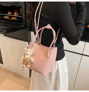 Detail of pink lychee textured bucket bag with a cute plush bear pendant and leather strap