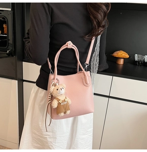 Detail of pink lychee leather bucket bag with teddy bear charm and sleek handles