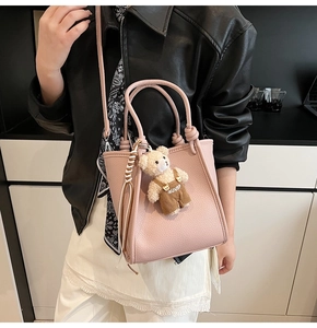 Pink bucket bag with litchi texture and cute teddy bear charm detail in a lifestyle setting