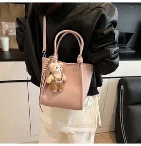 Détail d'un sac à main rose en cuir grainé avec pendentif ours et bandoulière amovible