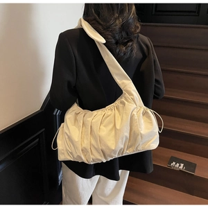 Close-up of the pleated nylon fabric and wide shoulder strap on the cream bucket bag