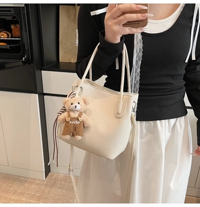 Detailed view of cream leather bucket bag with teddy bear pendant and adjustable strap
